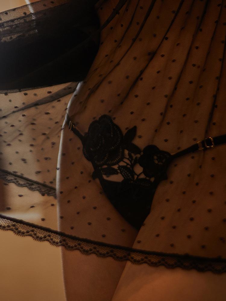 Sheer black lingerie with polka dot pattern and delicate floral lace detailing on the thong, enhancing feminine elegance.
