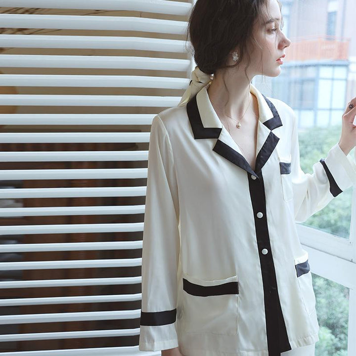 Silk pajama set featuring a cream top with black trim and buttons, shown on a model against a modern window backdrop.