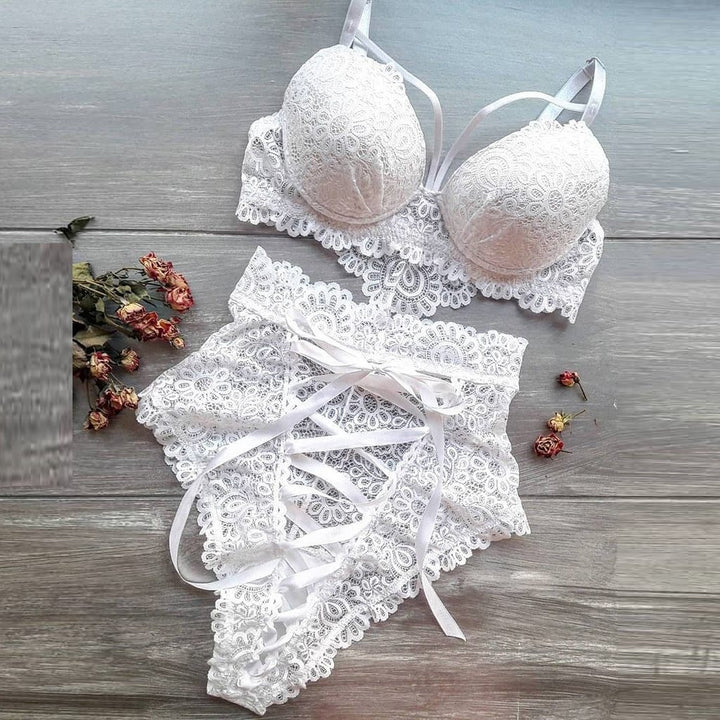 White lace lingerie set featuring a padded bra with intricate floral patterns and matching high-waisted bikini bottoms with ribbon detailing, styled on a wooden surface with dried flowers.