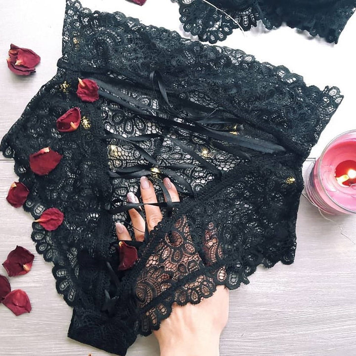 Black lace lingerie with delicate details and ribbon accents, adorned with rose petals and a candle.