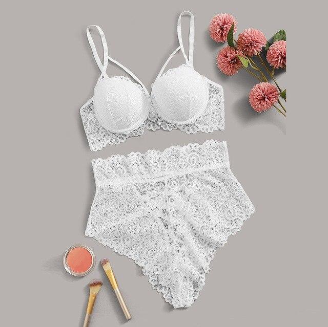 White lace lingerie set featuring a floral patterned bra with adjustable straps and matching high-waisted panties, styled with makeup items and flowers on a grey background.