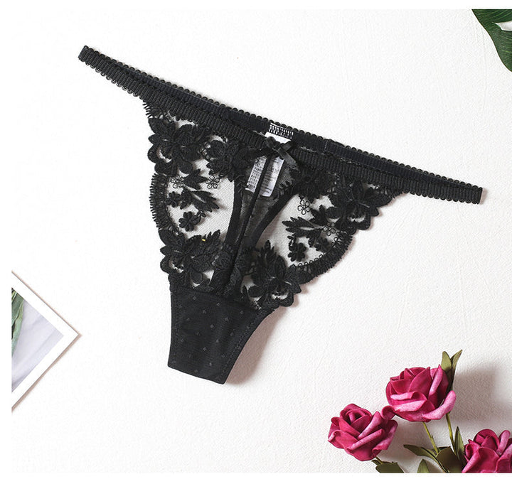 Black lace thong with intricate floral embroidery and polka dot detailing, elegantly displayed with roses on a light background.
