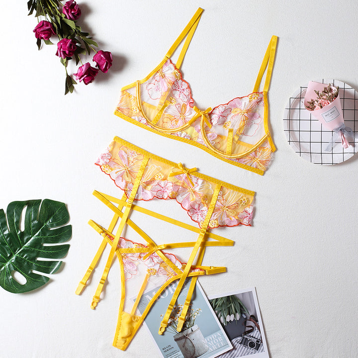 Yellow lace lingerie set with floral embroidery, featuring a bralette and matching thong with delicate straps, styled against a clean background with leaves and decorative items,