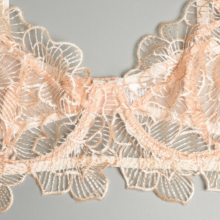 Lacey peach bra with floral embroidery and scalloped edges on a soft gray background.