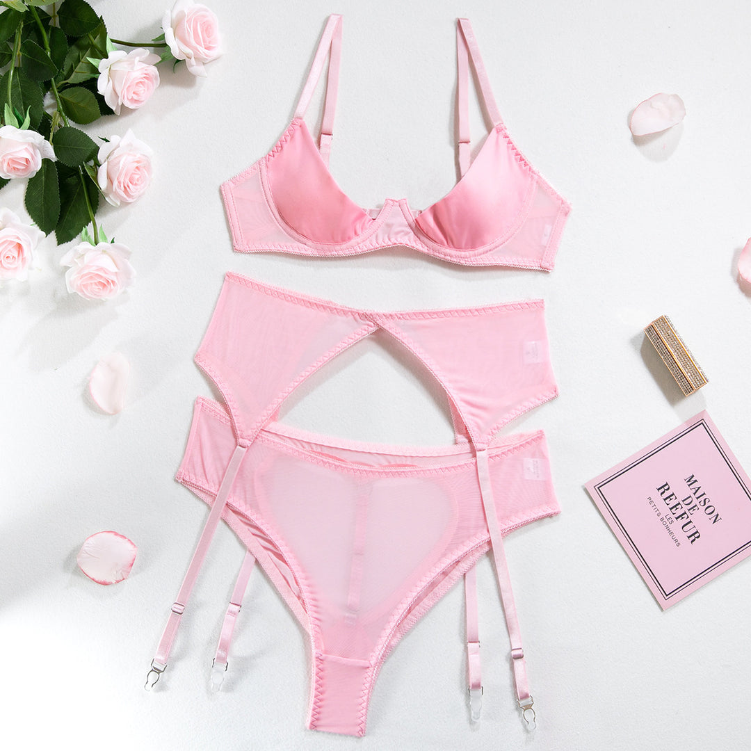 Pink lingerie set featuring a soft cup bra, matching panties with garter straps, and delicate lace detailing, beautifully arranged on a white background with roses and decorative items.