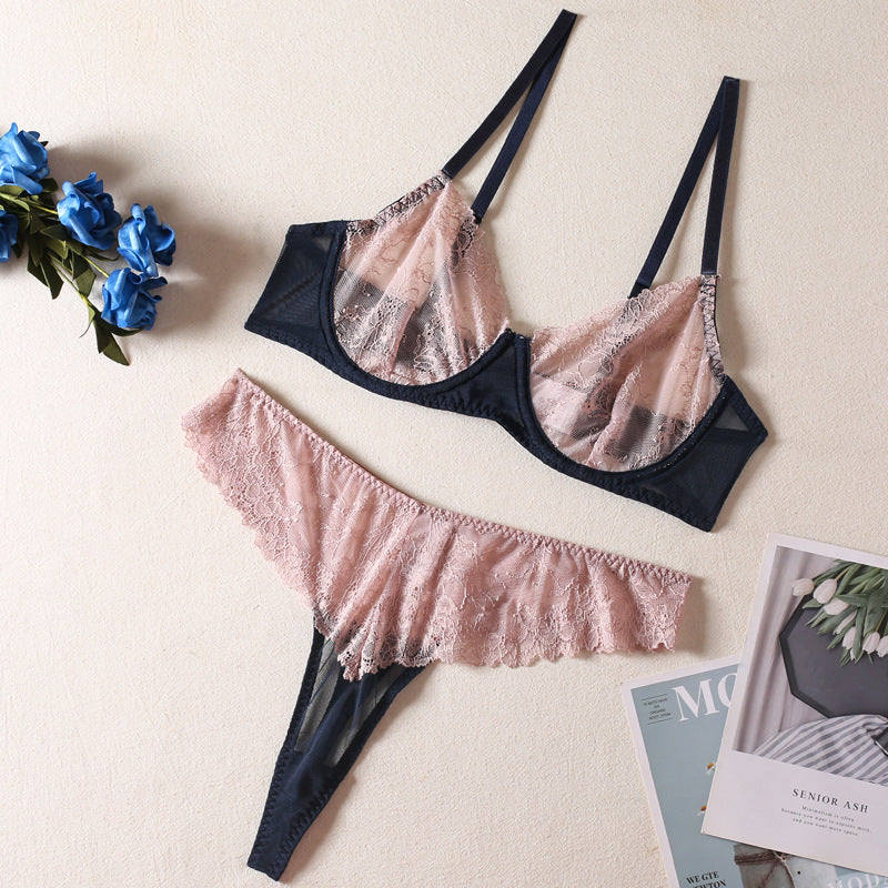 Lingerie set featuring a sheer lace bralette with navy straps and a matching pink lace thong, beautifully arranged with blue flowers and magazines in the background