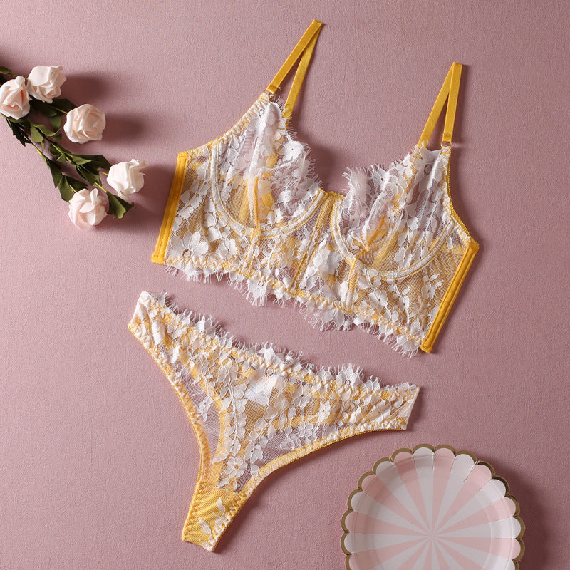 Yellow lace bralette and matching thong set with floral design on a pink background.