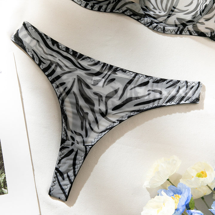 Sheer black and grey zebra print thong lingerie with delicate trimming, displayed on a light background with flowers.