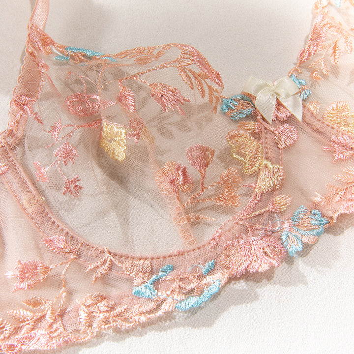 Delicate sheer bra with intricate floral embroidery in pastel hues and a small satin bow accent.