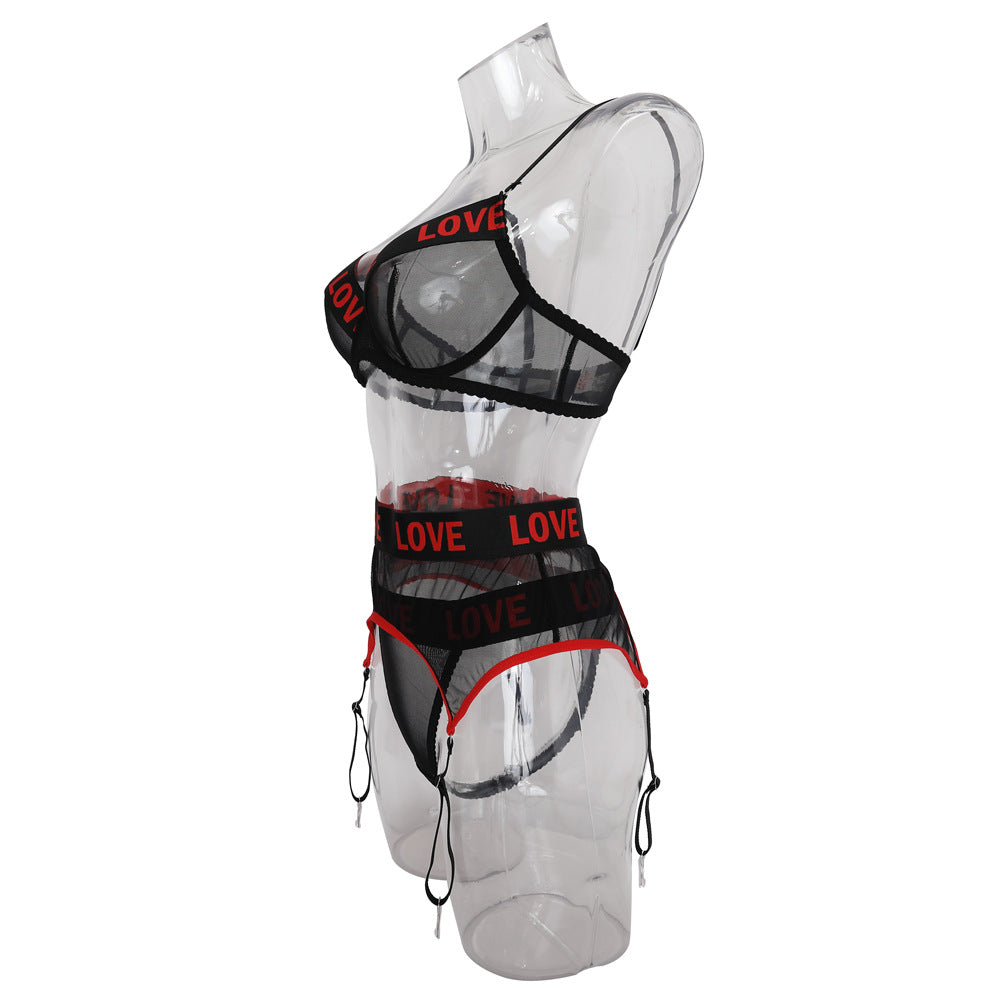 Black mesh lingerie set featuring red "LOVE" lettering, including a bralette and matching thong with garter straps, showcased on a clear mannequin for a