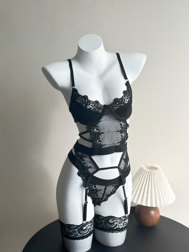 Black lace lingerie bodysuit displayed on a mannequin, featuring intricate floral lace detailing, adjustable straps, and a seductive design. The bodysuit includes