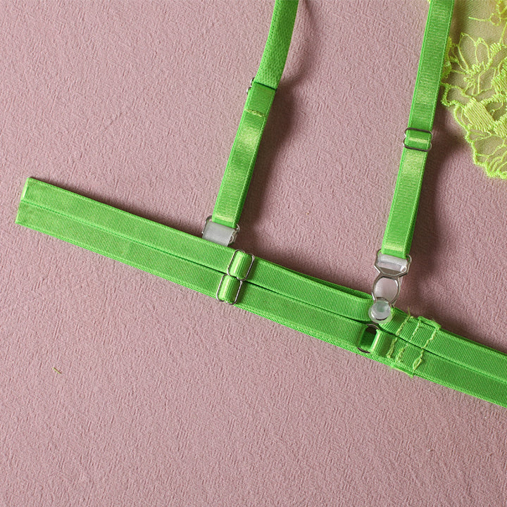 Neon green lingerie harness featuring adjustable straps and metal connectors on a textured pink background.