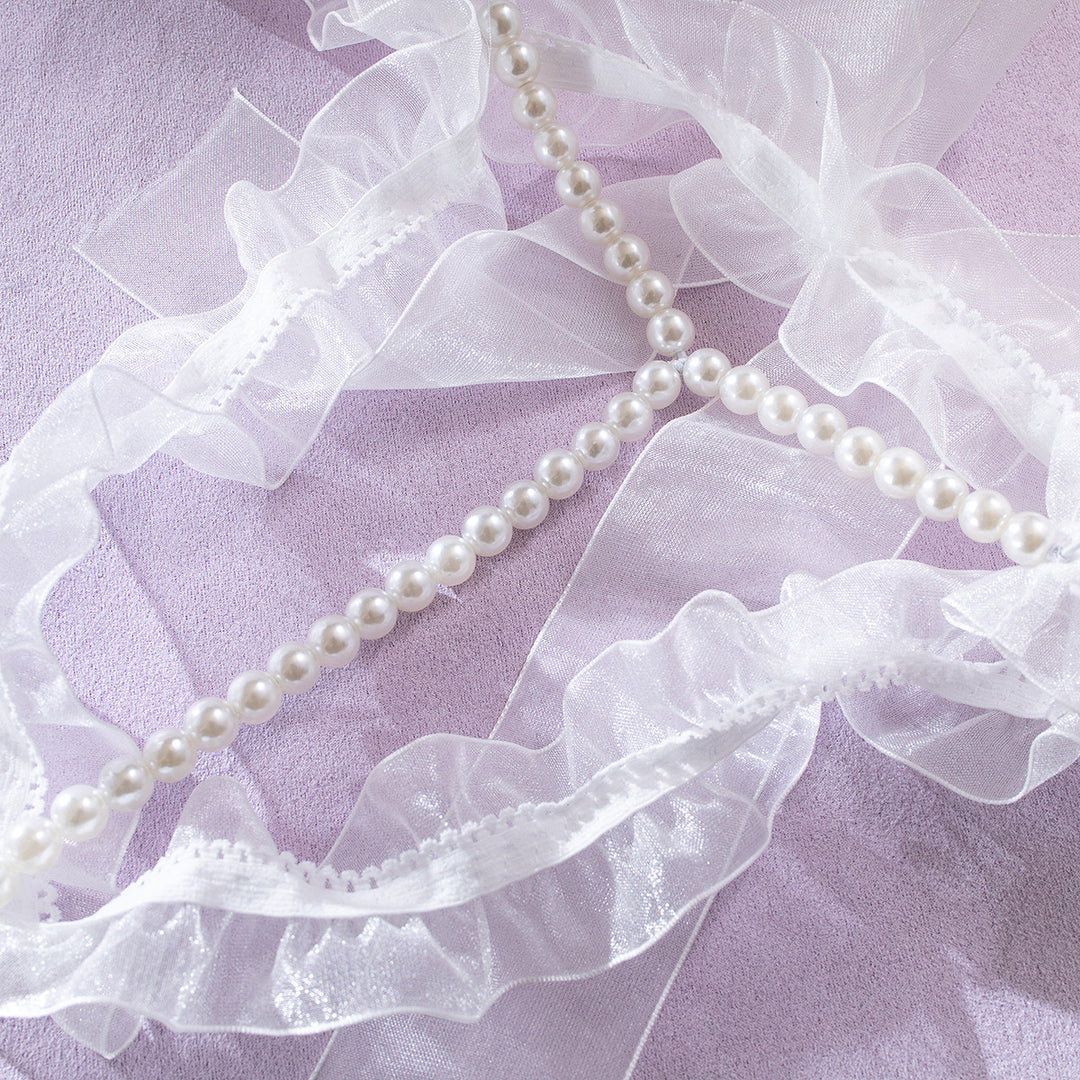 Delicate bridal lingerie accessories featuring sheer white ribbons and a strand of lustrous pearls, elegantly arranged on a soft lavender background, perfect for adding a touch