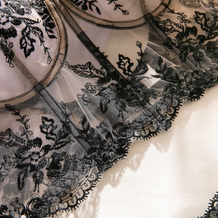 Black lace lingerie with intricate floral embroidery on a soft fabric background.