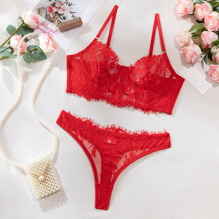 Red lace lingerie set featuring a bra with adjustable straps and a matching thong, elegantly styled with floral accents and a pearl handbag accessory, surrounded by pink roses