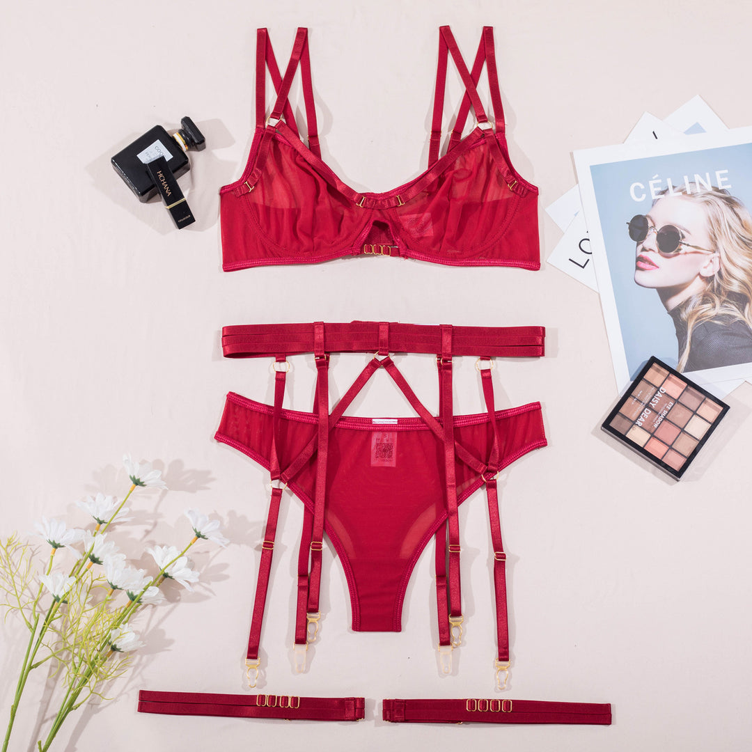 Elegant red lingerie set featuring a sheer bra with multiple straps, a matching thong with garter attachments, and delicate gold accents. Styled with a chic perfume