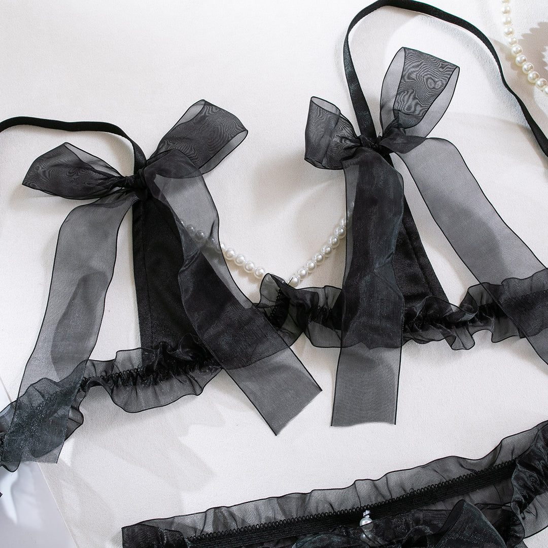 Sheer black lingerie set featuring delicate bows and ruffled edges, complemented by a string of pearls, perfect for a romantic occasion or special night. Elev