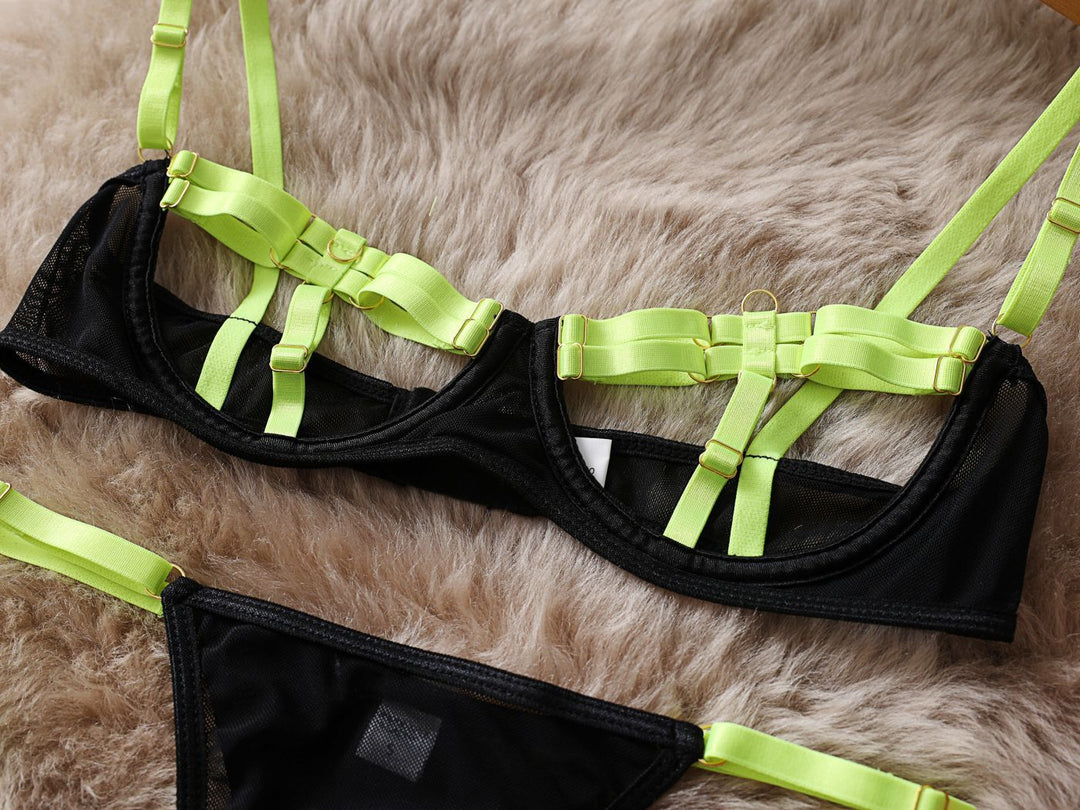 Black lingerie set with neon green straps featuring a mesh bralette and matching thong, displayed on a fluffy surface.