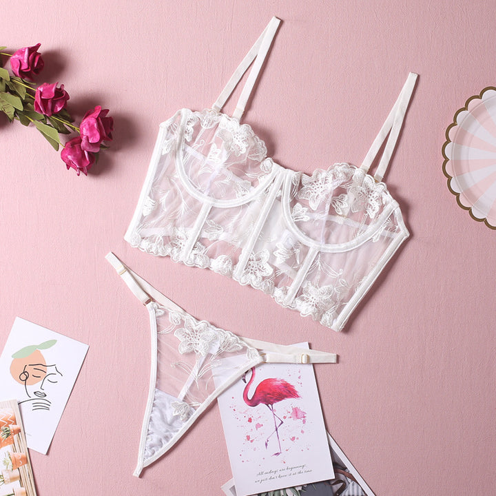 Lace lingerie set featuring a sheer white bralette with floral embroidery and adjustable straps, paired with matching white thong underwear. The elegant design is displayed against