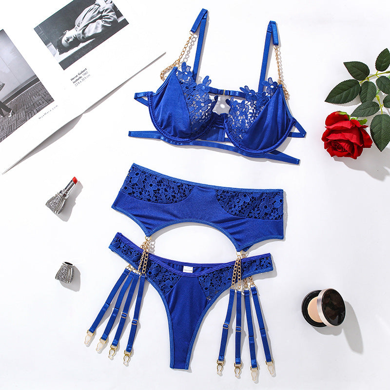 Blue lace lingerie set featuring a bralette with floral detailing and matching bottoms with chain accents, styled on a white background with beauty accessories.