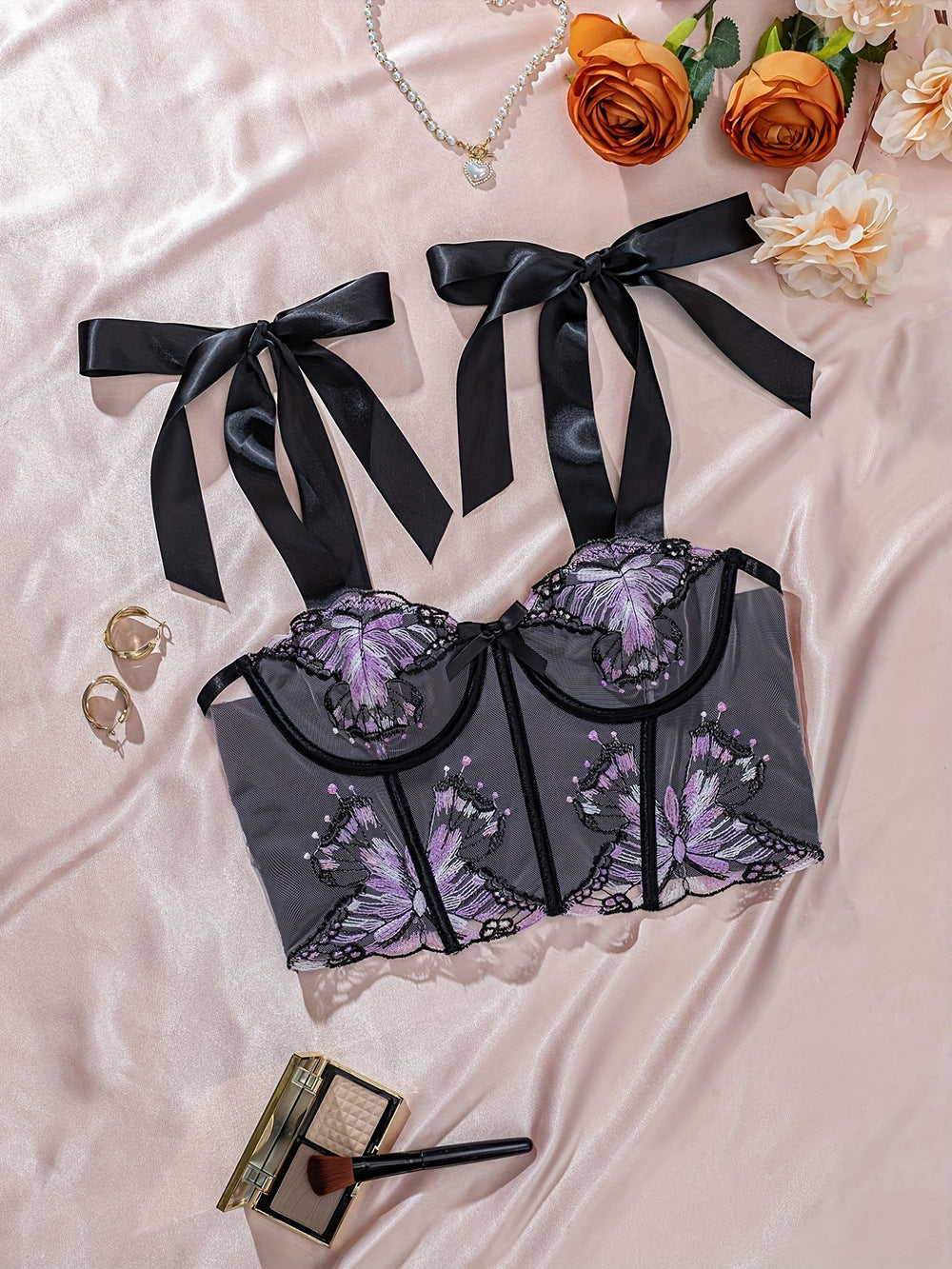 Lace bralette with intricate butterfly embroidery in shades of purple, featuring elegant satin ribbons, styled on a soft satin backdrop with decorative flowers and jewelry,