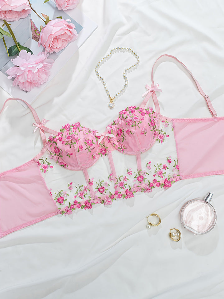 Pink embroidered lingerie set featuring delicate floral designs, complemented by soft satin and sheer fabric, styled with accessories like a pearl necklace and floral decor, perfect for