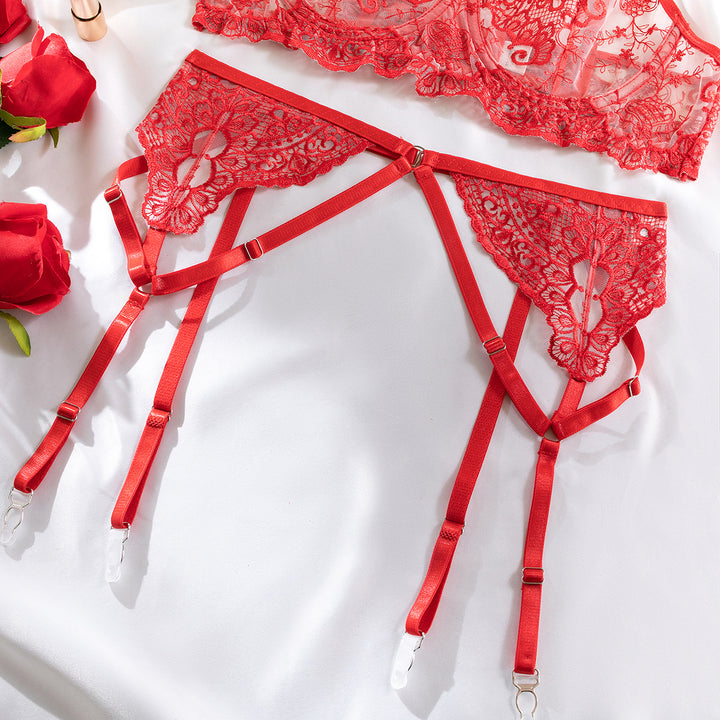 Red lace garter belt with adjustable straps, featuring intricate floral design and satin accents, displayed with roses on a soft fabric background.