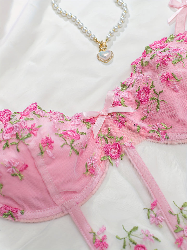 Pink embroidered lingerie set featuring delicate floral designs, accented with satin ribbons. The set is styled with a sheer fabric that adds a touch of elegance, complemented