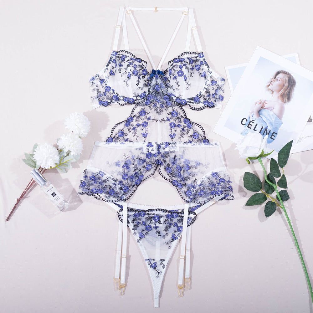 Lace lingerie set featuring floral embroidery in shades of blue, with a delicate bralette, matching panties, and garter belt, styled elegantly with accessories.