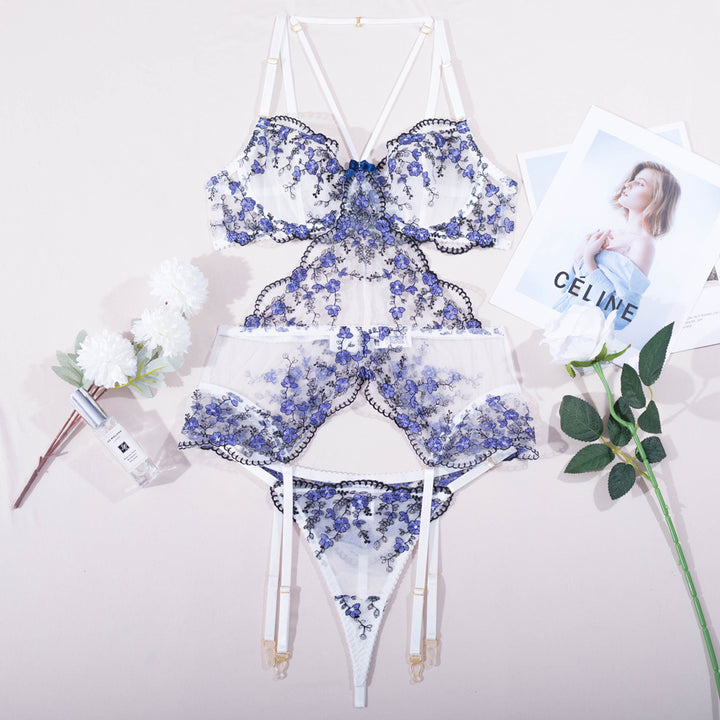 Luxe floral lace lingerie set featuring intricate blue embroidery, a delicate bralette with satin tie, matching sheer panties, and garter straps, styled elegantly