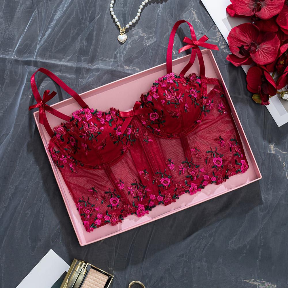 Luxe red lace bra with floral embroidery displayed in a pink gift box, featuring delicate satin bows on the straps, surrounded by floral accents and elegance in