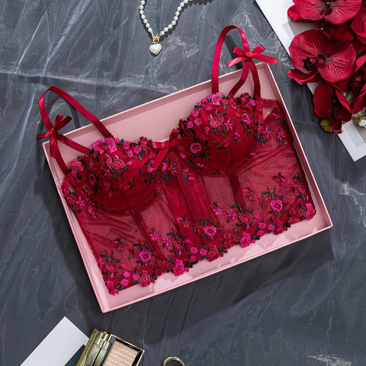 Luxe red lace bra with floral embroidery displayed in a pink gift box, featuring delicate satin bows on the straps, surrounded by floral accents and elegance in