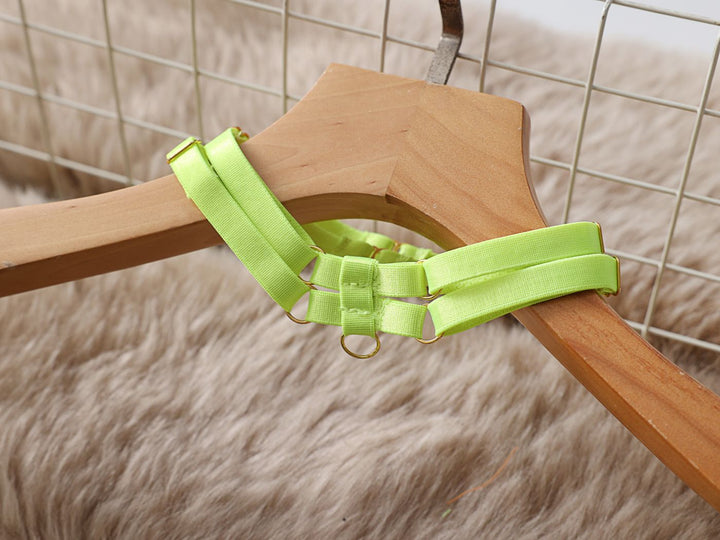 Neon green lingerie harness displayed on a wooden hanger against a soft textured background.