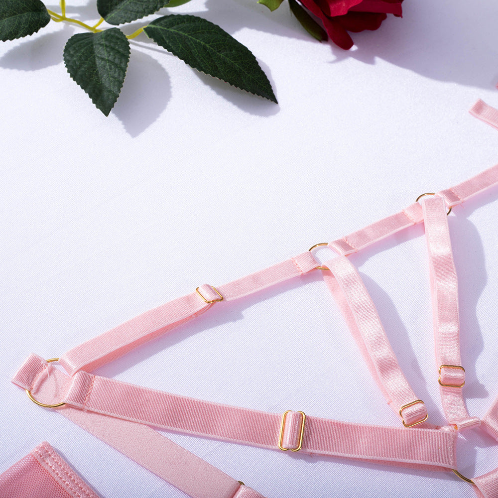 Delicate pink lingerie straps with gold hardware laid out on a white fabric surface, accompanied by a red rose and green leaves, showcasing a luxurious and romantic