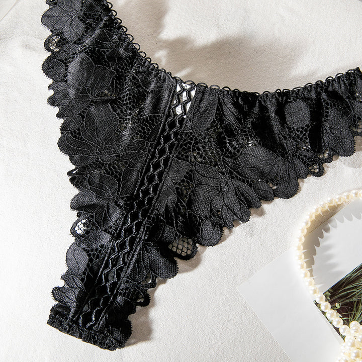 Black lace thong featuring floral patterns and delicate detailing, styled on a soft surface with pearl accessories.