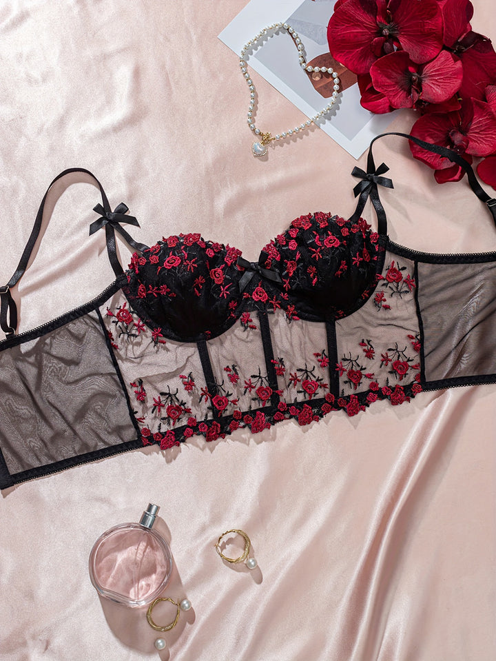 Black lace lingerie set with floral embroidery, featuring underwire cups and sheer mesh panels. Styled with elegant bows on straps, displayed against a soft satin background