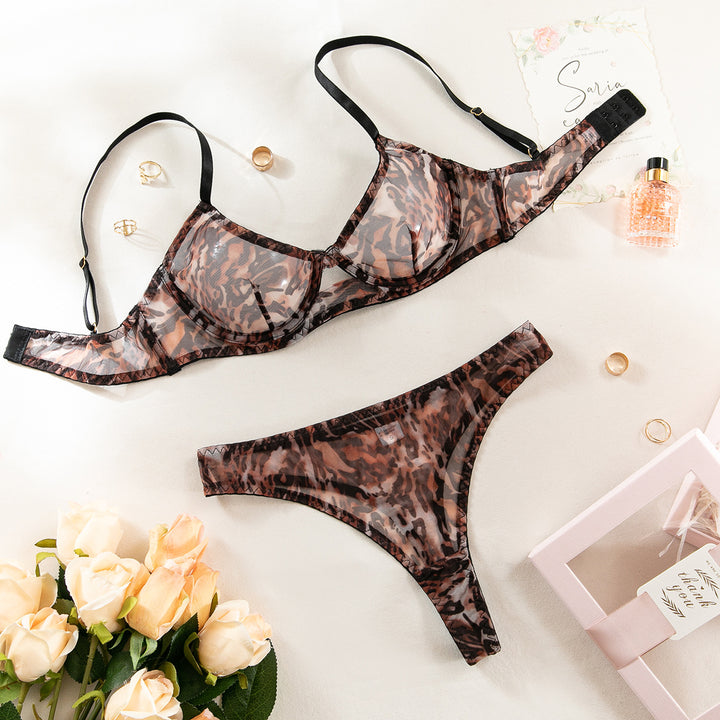 Luxe sheer leopard print lingerie set featuring a padded bra and matching thong, complemented by gold rings and a floral bouquet on a soft background, perfect for