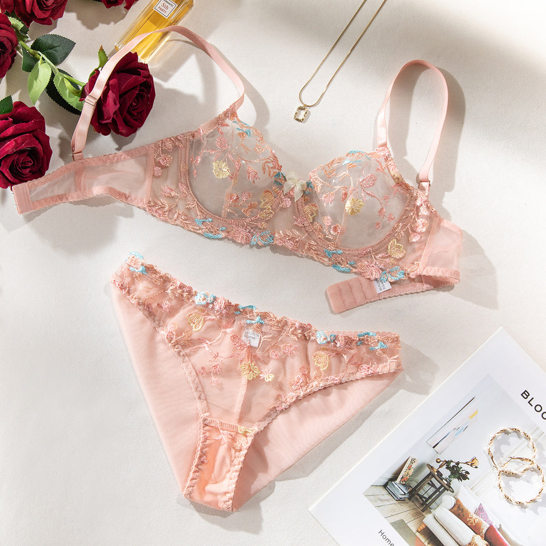 Lingerie set featuring a sheer peach bra with delicate floral embroidery and matching panties, elegantly styled with roses and accessories for a romantic touch.