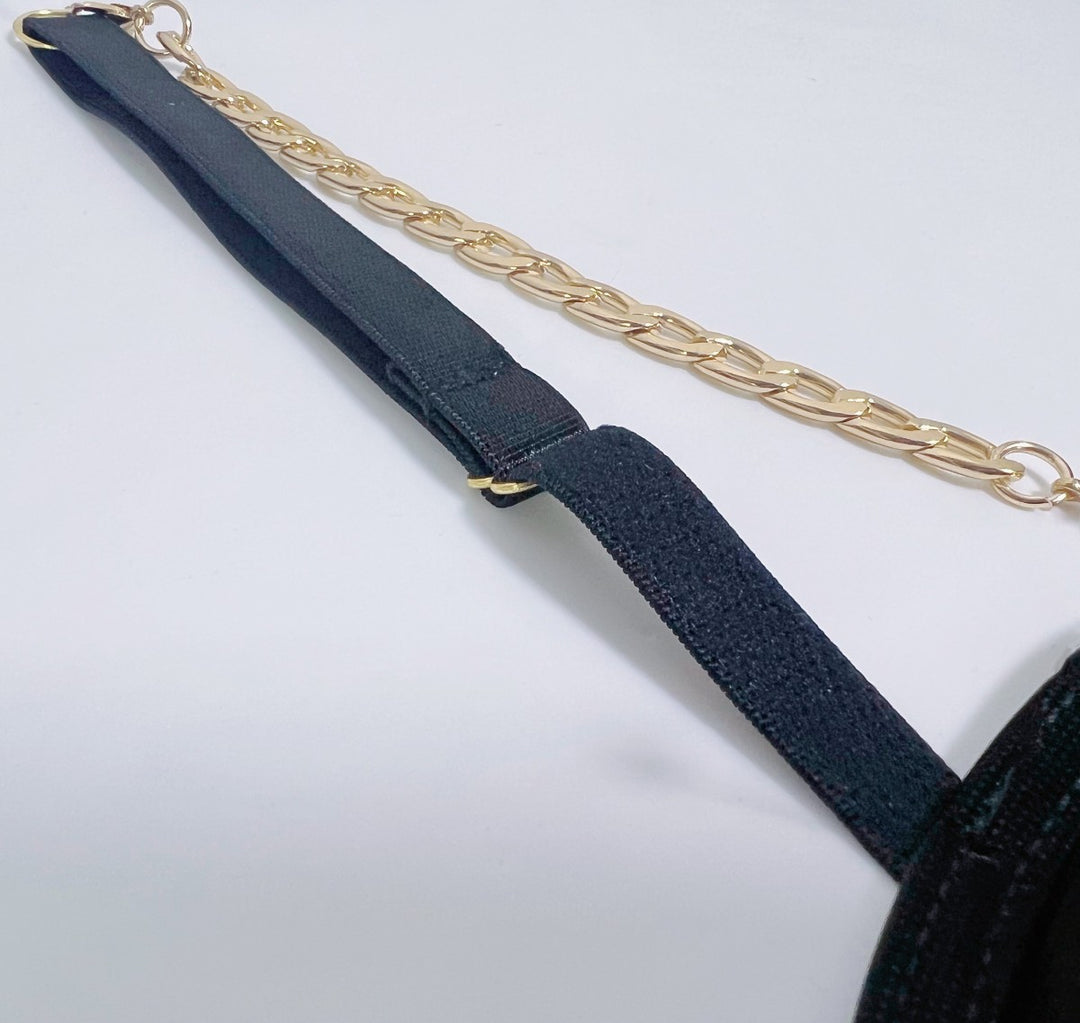 Close-up of a black lingerie strap with a gold chain accent.