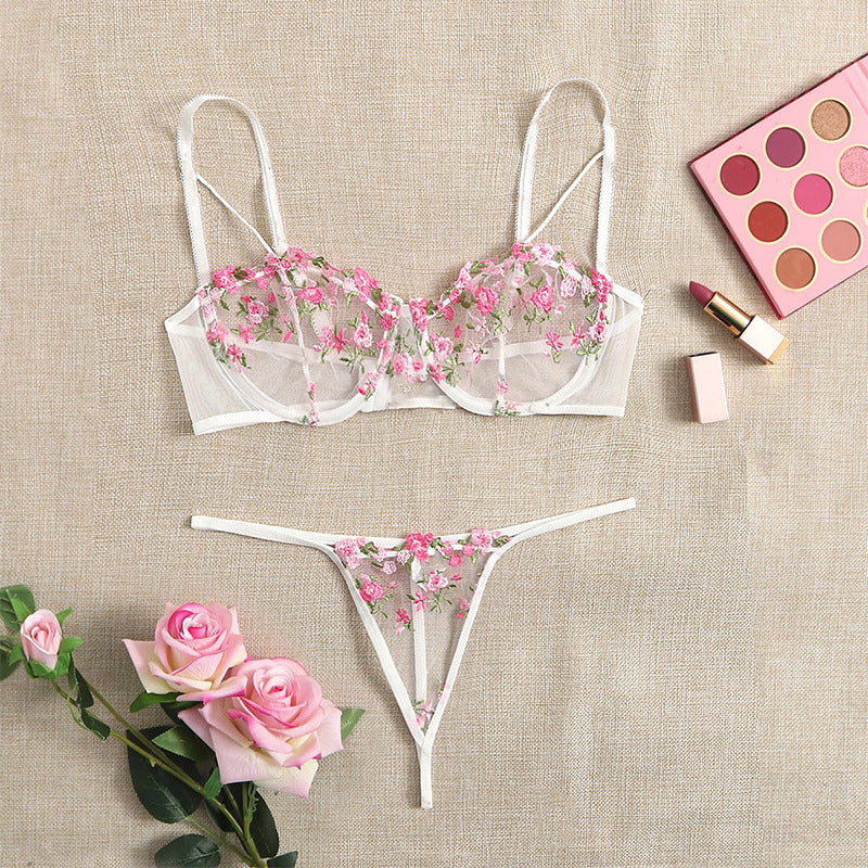 Lingerie set featuring a delicate sheer floral embroidered bra and matching thong, elegantly displayed on a textured background with pink roses and makeup products, perfect for