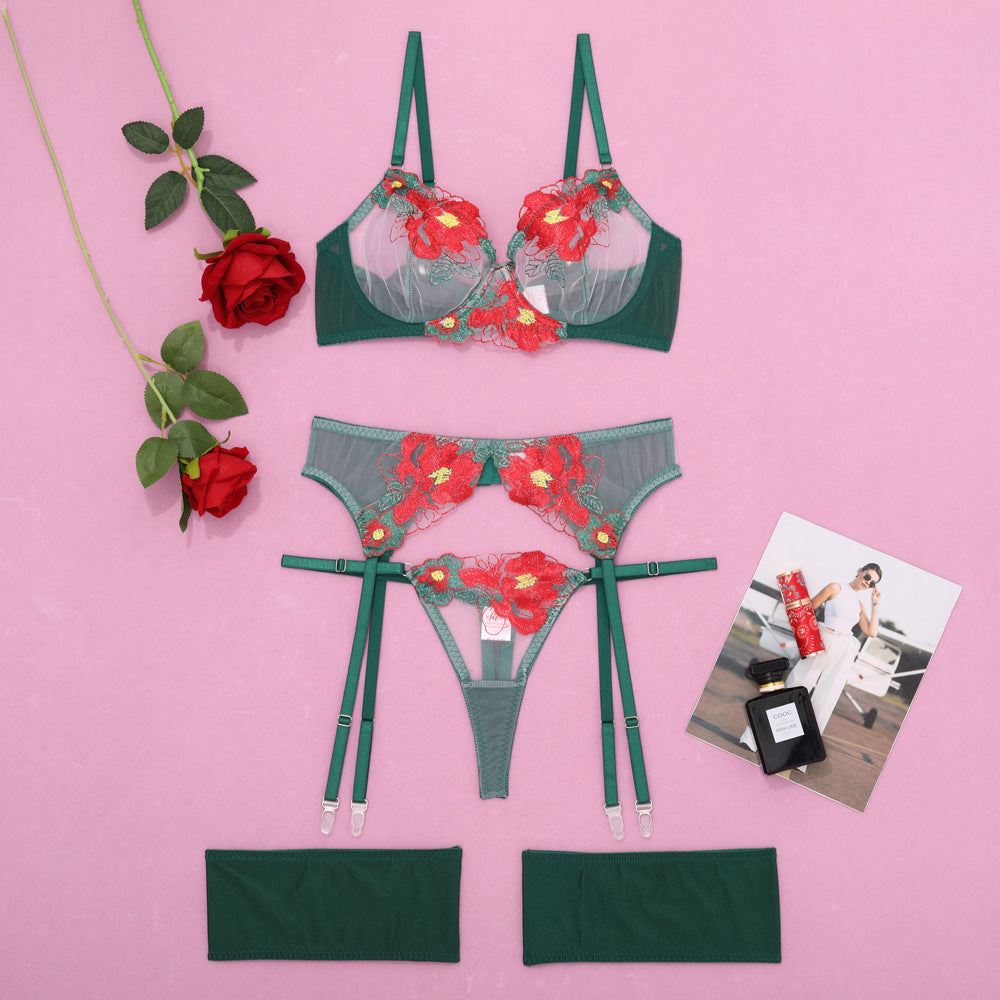 Green lingerie set with floral lace detailing, featuring a bra and matching thong, accompanied by two fabric harnesses and styled with red roses and a fashion magazine.