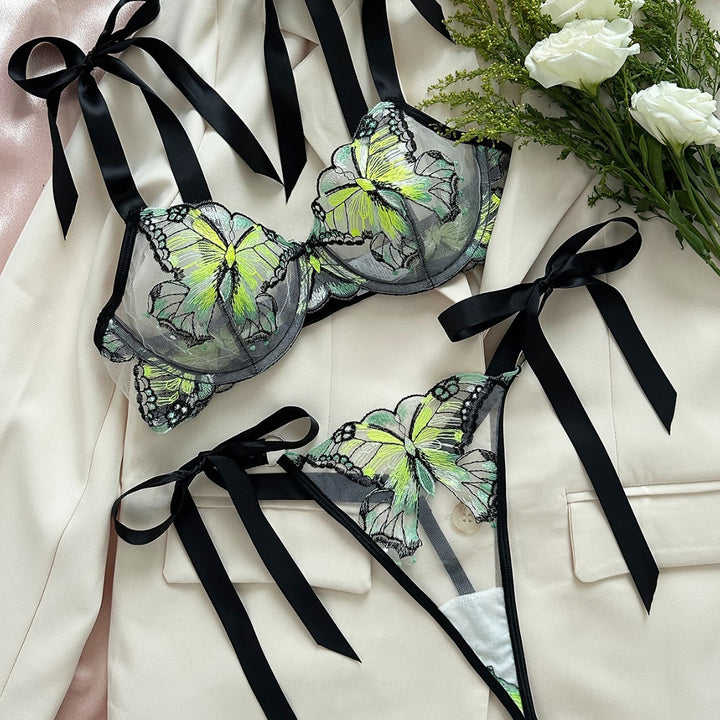 Elegant lingerie set featuring a black mesh bra and matching thong, adorned with vibrant butterfly embroidery in shades of green and yellow. The bra has delicate black satin