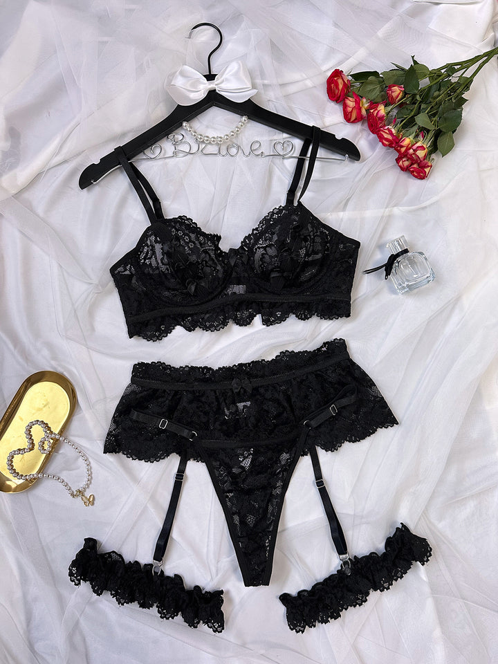 Luxe black lace lingerie set featuring a floral bralette, matching thong, and garter belt, styled with ruffled thigh straps, finished on a