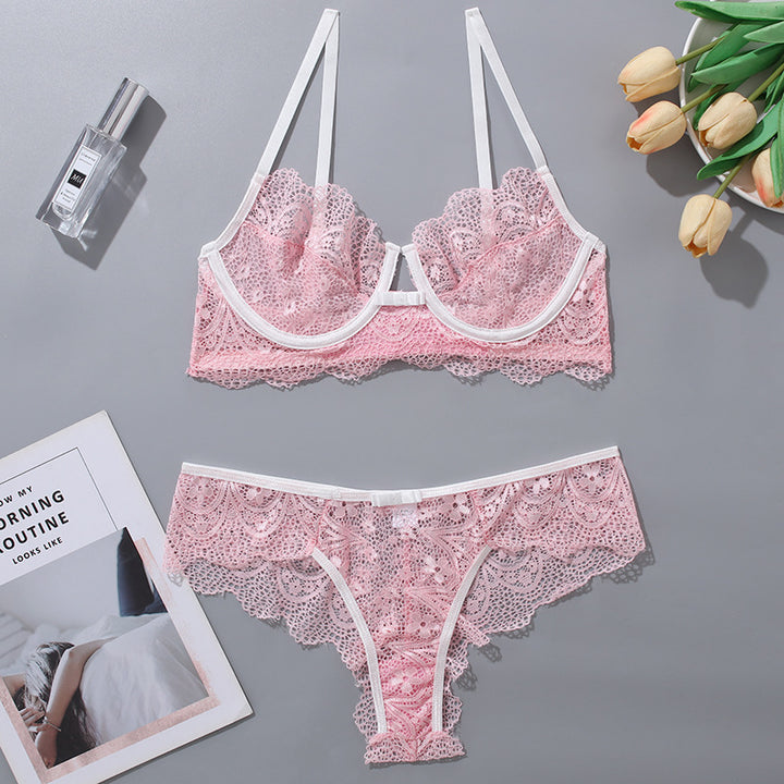 Pink lace lingerie set featuring a bralette and matching thong, embellished with delicate scalloped edges and white trim, styled on a gray background with complementary accessories.