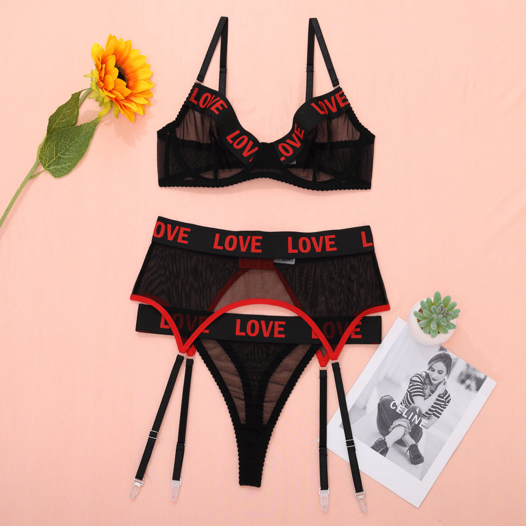 Black lingerie set featuring a sheer bralette with 'LOVE' printed straps and matching sheer panties, styled with red accents against a pastel background.