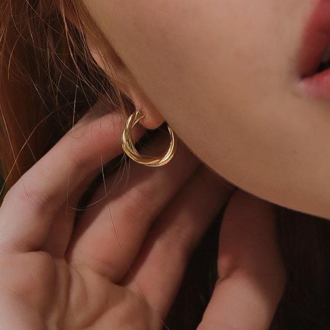 Gold hoop earrings displayed on a model's ear, highlighting a textured design and a soft, natural look.