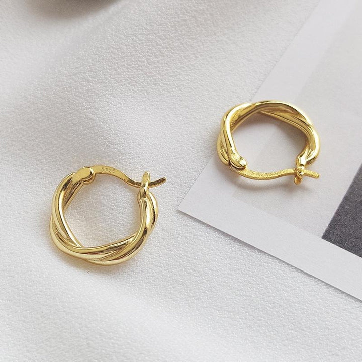 Gold twisted hoop earrings displayed on a soft fabric background.