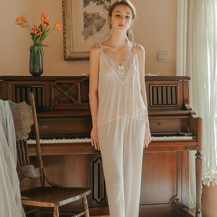 Elegant women's silk nightwear set featuring a lace detailed cami top and soft pants, displayed in a cozy room setting with a piano and floral decor.