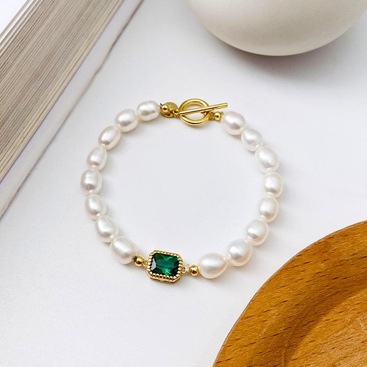 Elegant pearl bracelet featuring a central emerald-green gemstone and a gold toggle clasp, perfect for enhancing any outfit.