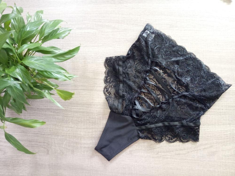 Black lace lingerie set featuring intricate detailing and ribbon accents, displayed on a light wood surface with a green plant.